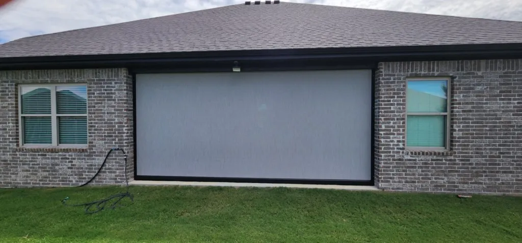 Wide motorized retractable screen closed over a brick ranch home patio in Northwest Arkansas