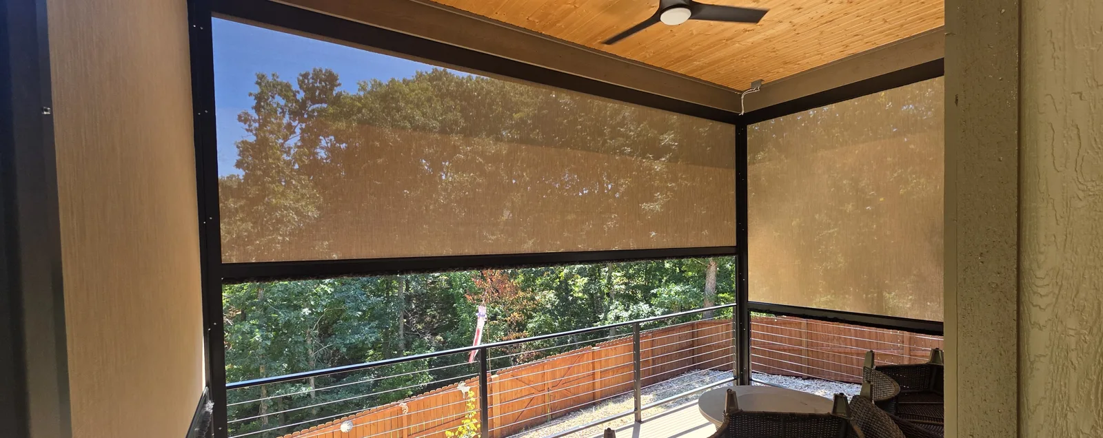 Two tan motorized retractable screens closed on a covered deck with a wood ceiling and cable railing in Latheron, Bella Vista, Arkansas