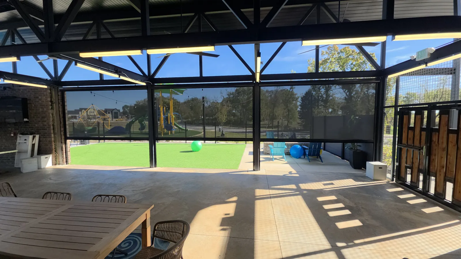Inside view of dark mesh screens across a steel-framed pavilion patio with a turf lawn beyond in Aurora, Bentonville, Arkansas