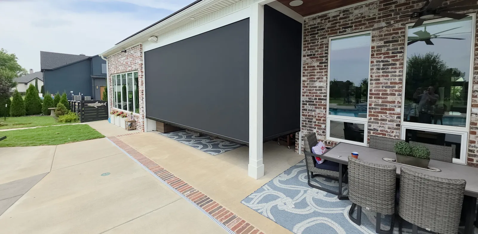 Charcoal screen closed beside a covered patio with outdoor seating and brick in Averie Estates, Cave Springs, Arkansas