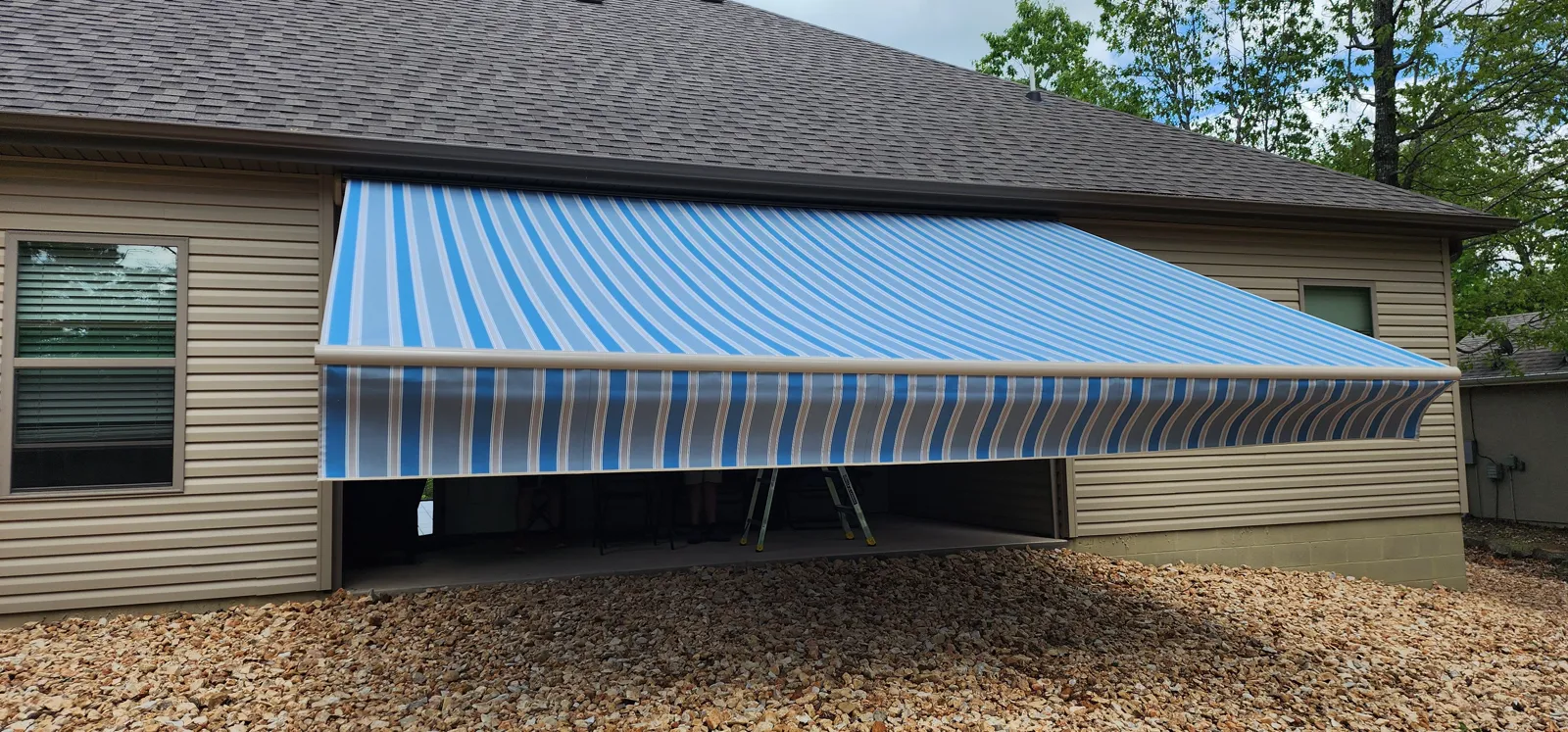 Blue and white striped retractable awning on a tan vinyl sided house in Berkshire, Bella Vista, Arkansas