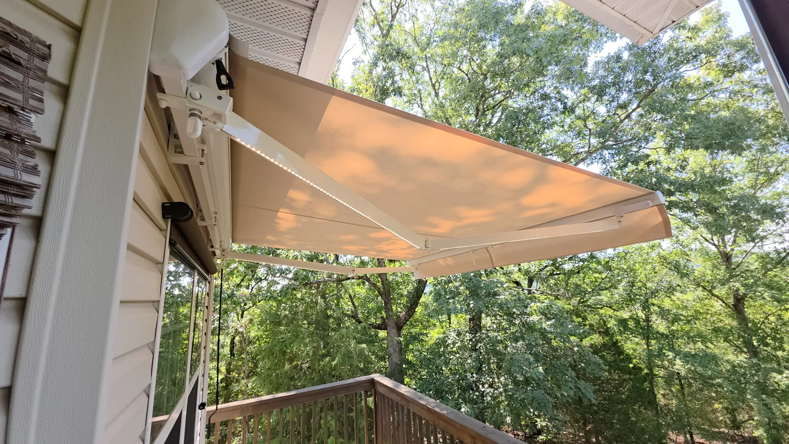 Tan retractable awning with white arms and an LED strip over a deck with trees behind in Birmingham, Bella Vista, Arkansas