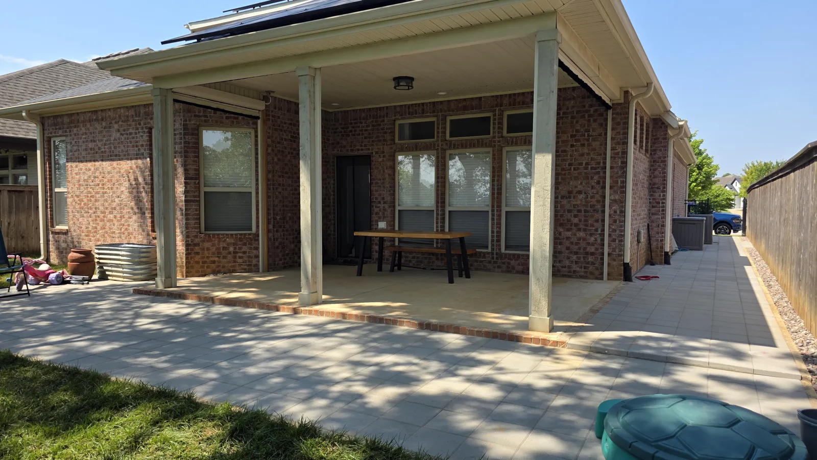 Covered back patio on a brick house with light-colored posts and a paver patio in Brighton Cottages, Bentonville, Arkansas