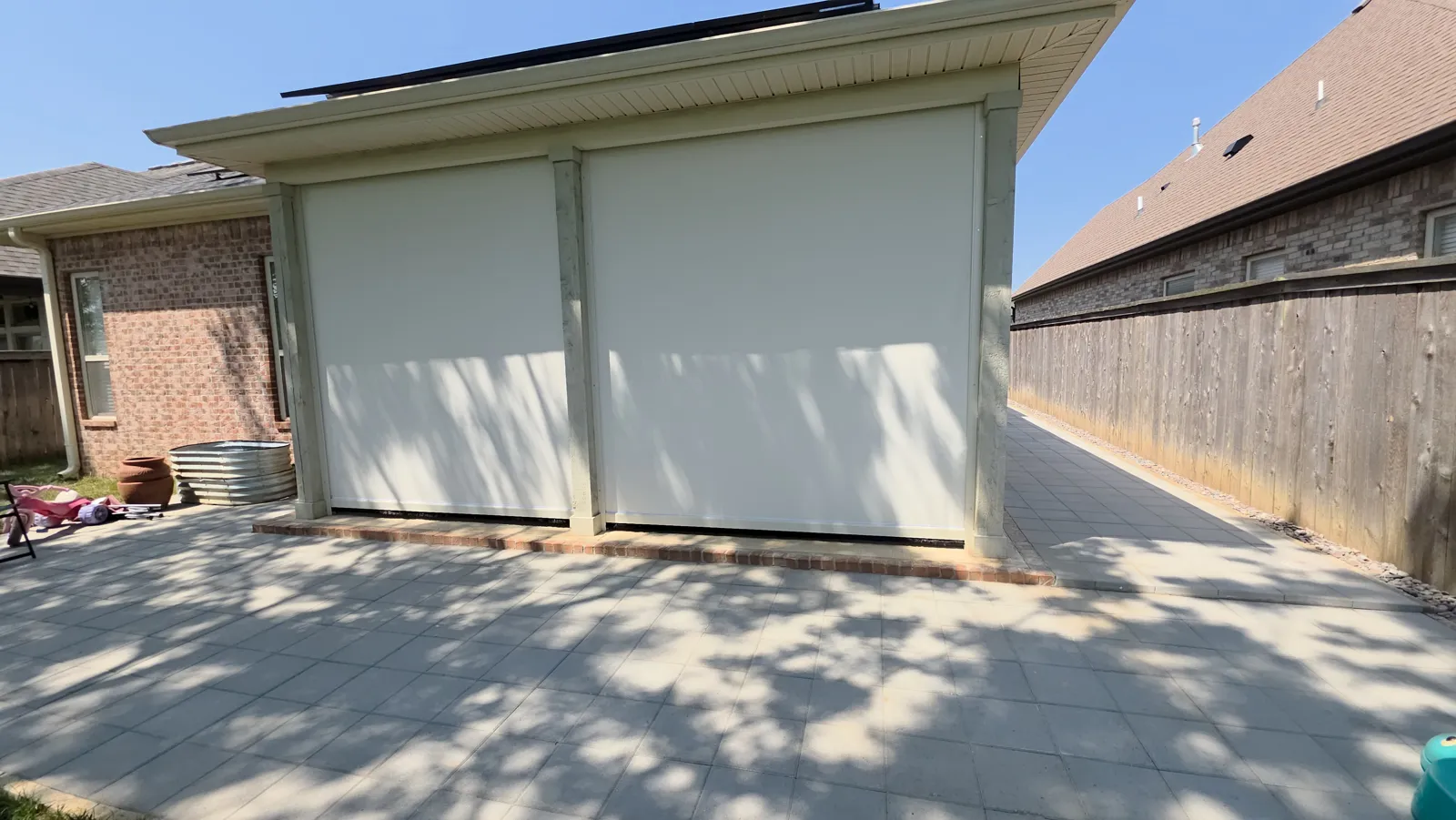 Two white screens closed across a garage-size opening on a house with a brick side and a wood fence, retractable screens for homes in Richards Glen, Little Flock, Arkansas