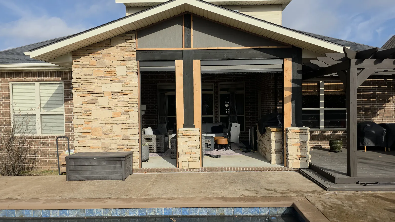 Dark screens rolled up under the gable of a covered patio with stone columns and cedar posts in Central Park, Bentonville, Arkansas