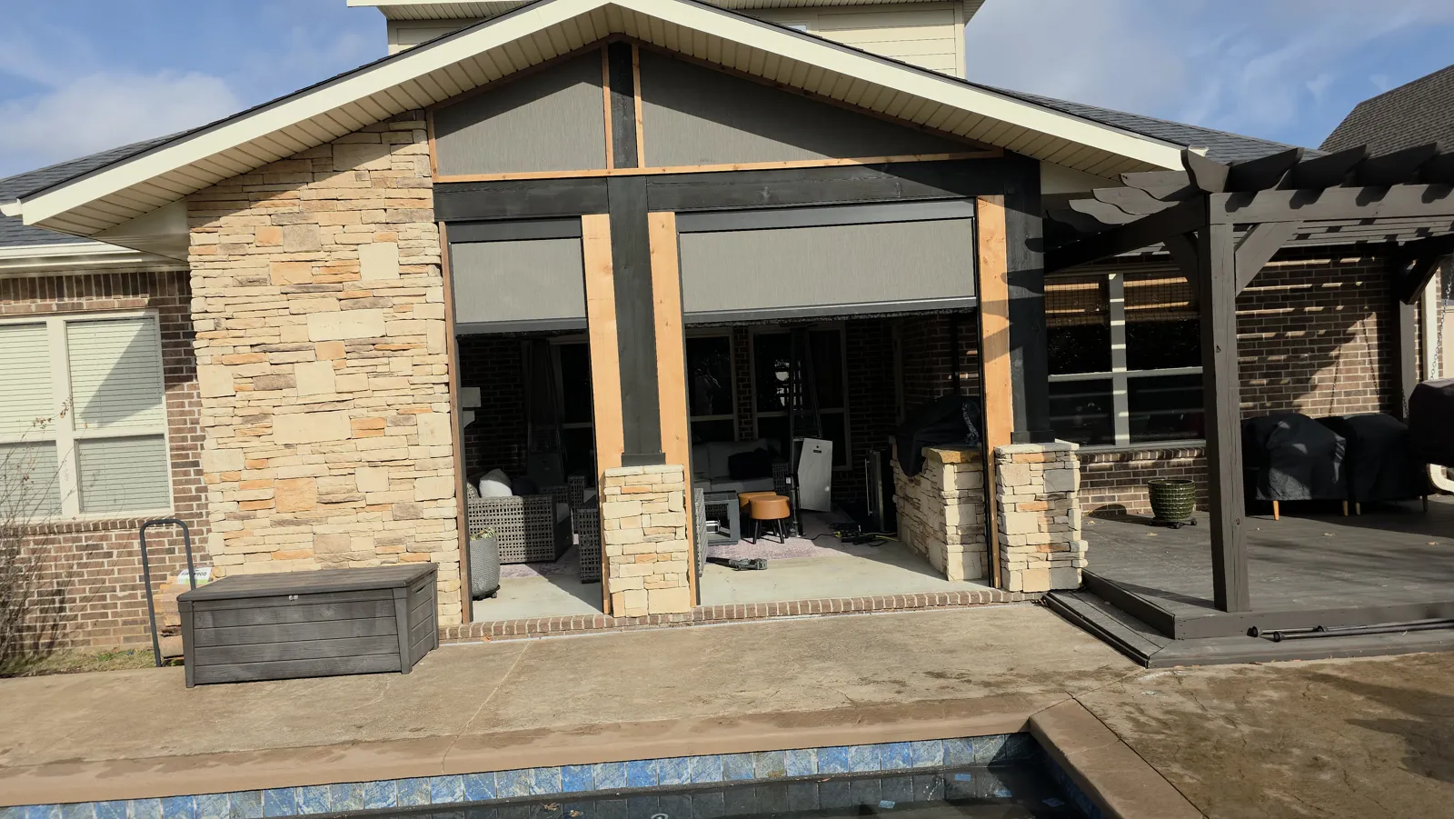 Gabled covered patio with stone columns and cedar posts and a pool edge in front in Central Park, Bentonville, Arkansas