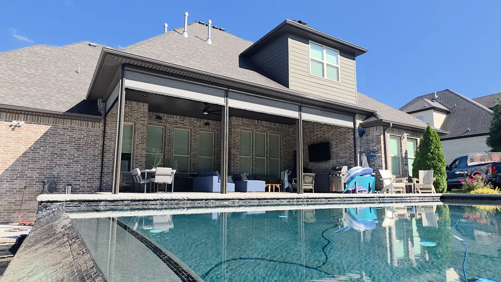 Gray screens rolled up under a covered brick back patio with a pool in front in Chapel View, Fayetteville, Arkansas