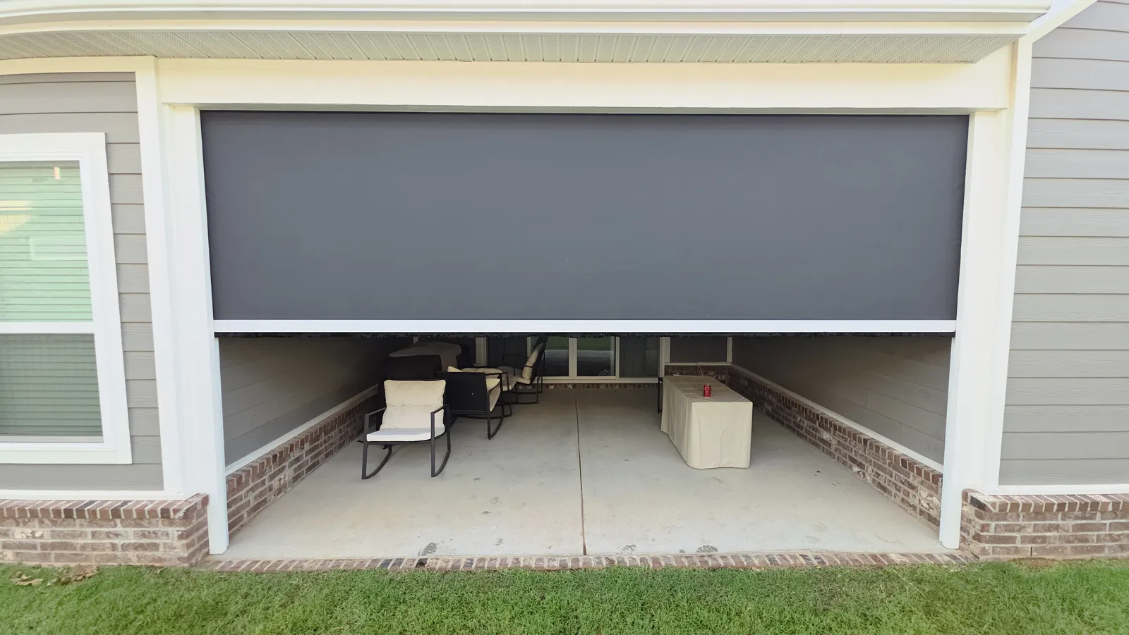 A dark gray screen lowered over a covered patio on a gray sided house with a brick base and white trim, retractable screens for homes in Cottages at the Park, Springdale, Arkansas