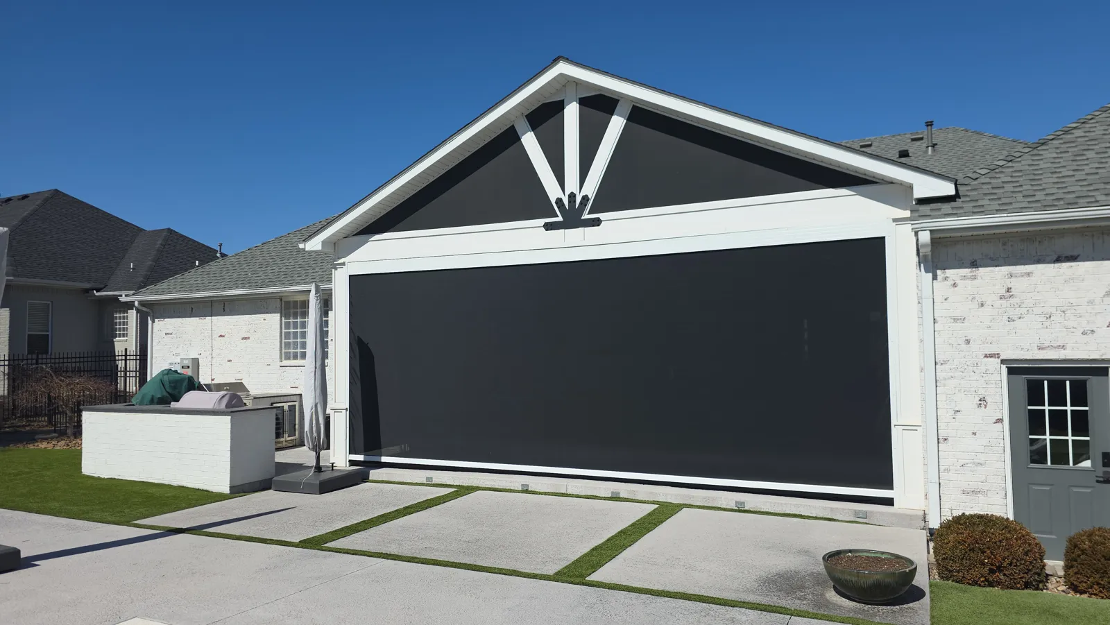 A dark screen closed across a gabled patio on a white painted brick house with a gray door and an outdoor kitchen, retractable screens for homes in Bridlewood, Springdale, Arkansas