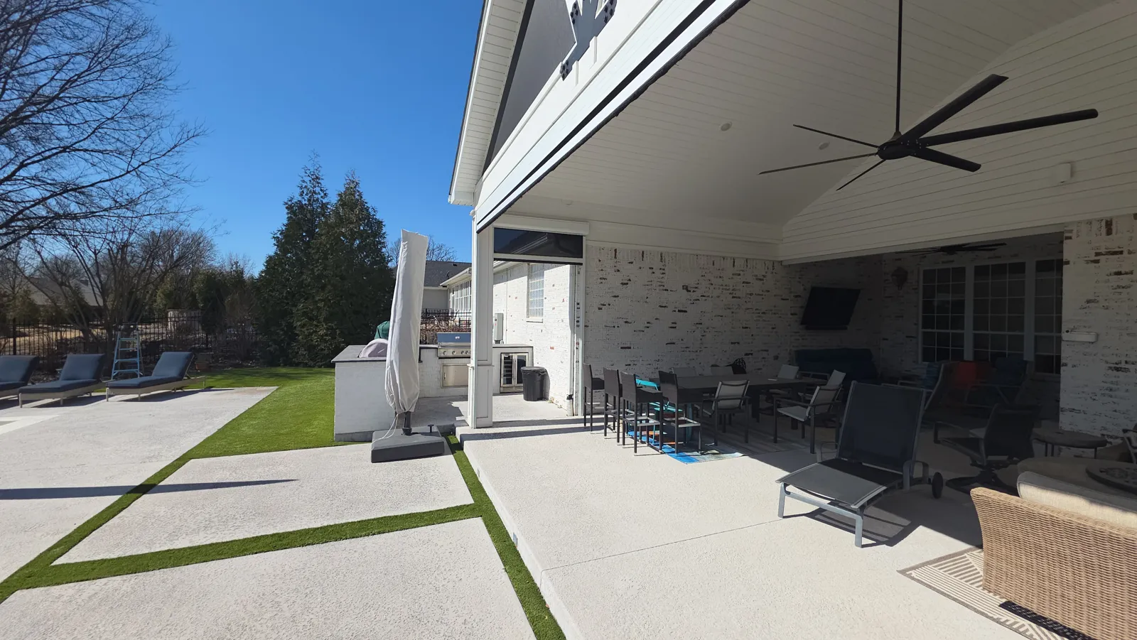 Inside view of a covered patio with a ceiling fan, black screen rolled up, turf strips outside in Elm Valley, Elm Springs, Arkansas