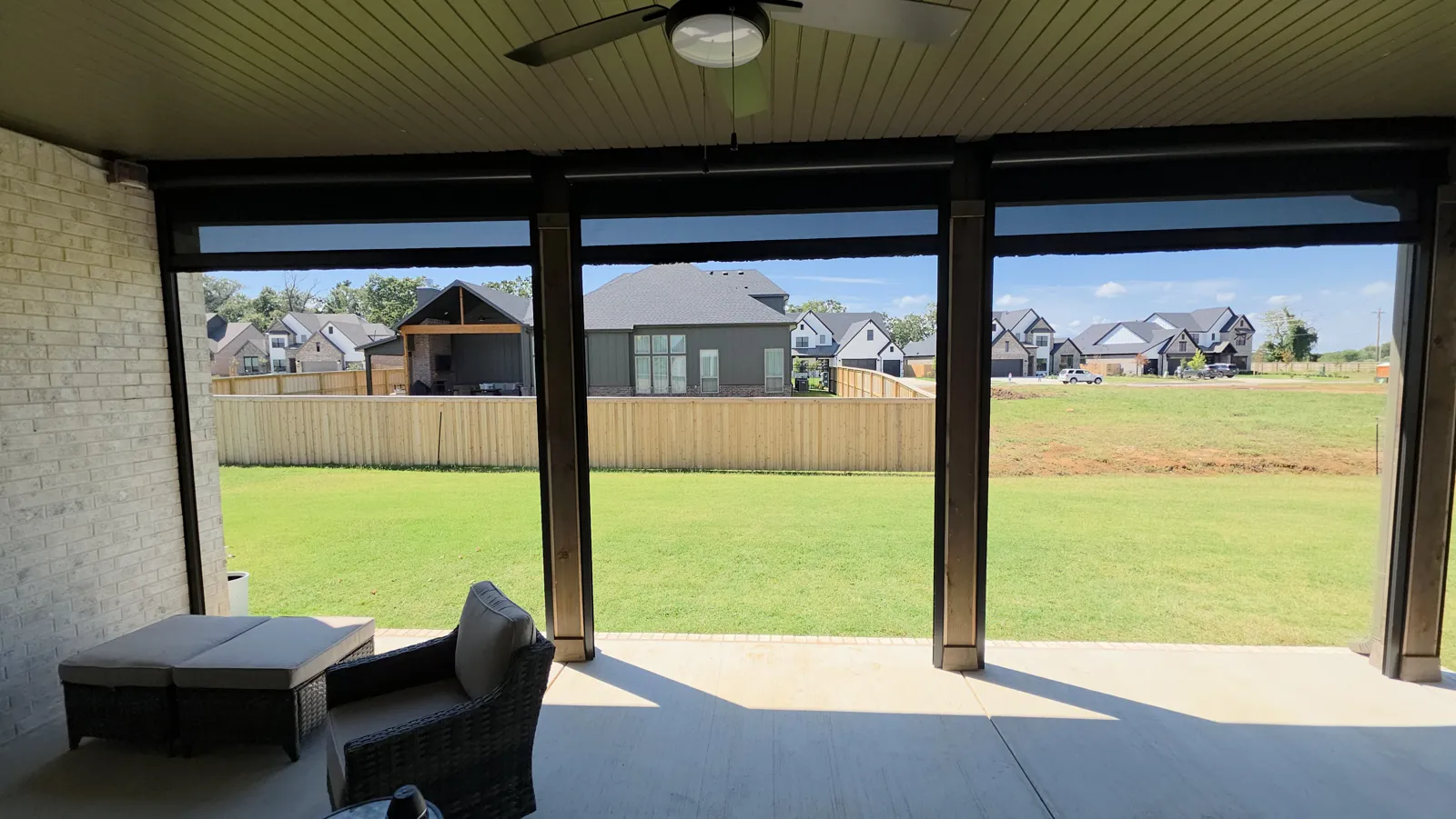 Dark screens rolled up under the ceiling of a covered patio looking out to the lawn and fence in Evening Star, Cave Springs, Arkansas