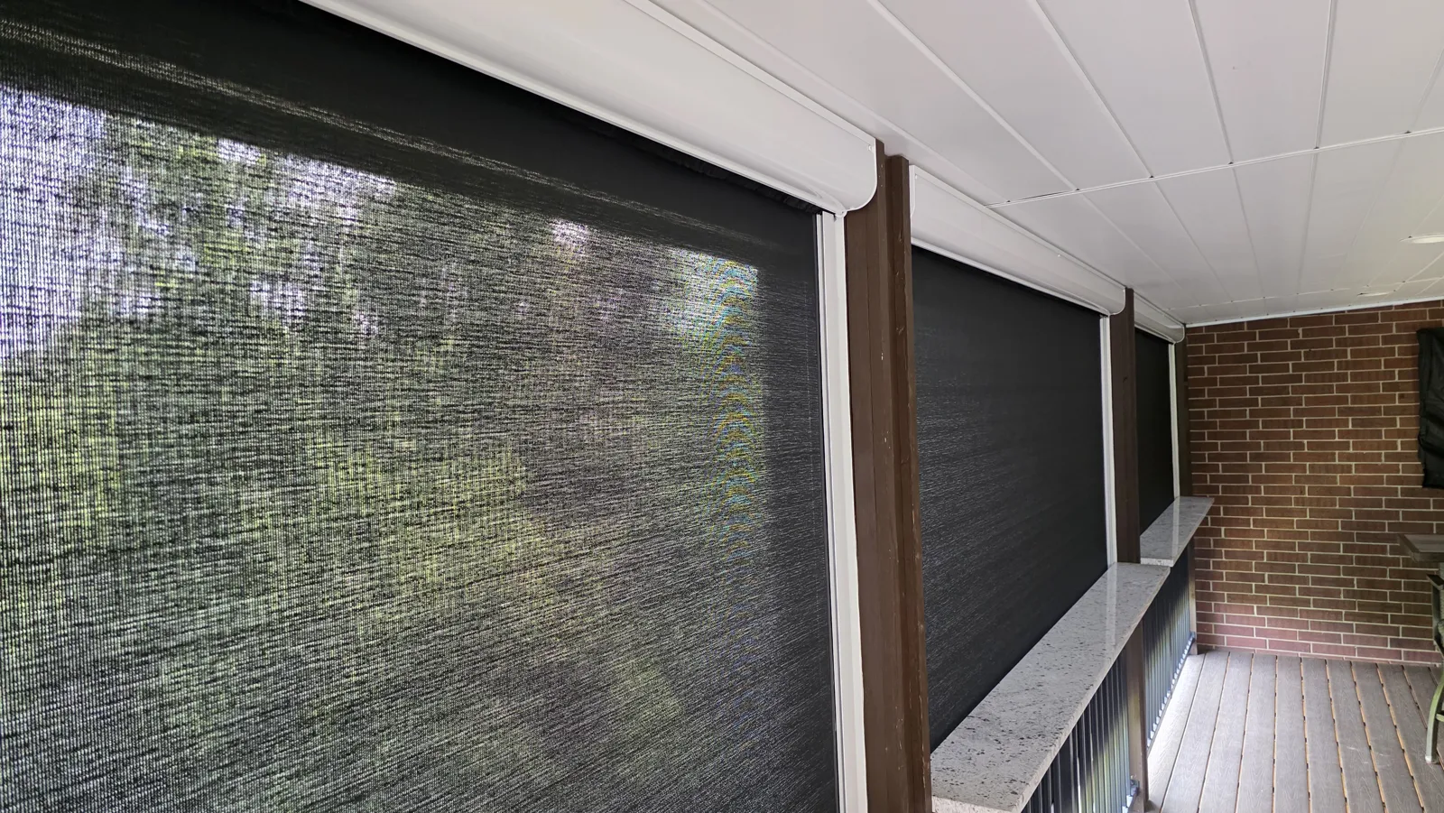 Dark open-weave mesh closed across a covered porch with a white ceiling and brick wall in Heathrow, Bentonville, Arkansas