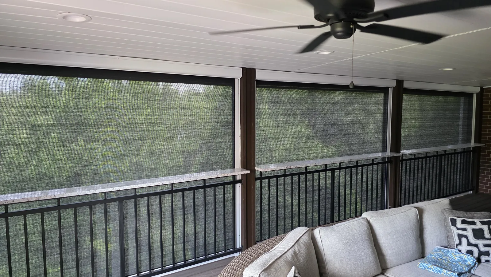 Inside view through dark mesh on a covered porch with a ceiling fan and sectional in Heathrow, Bentonville, Arkansas