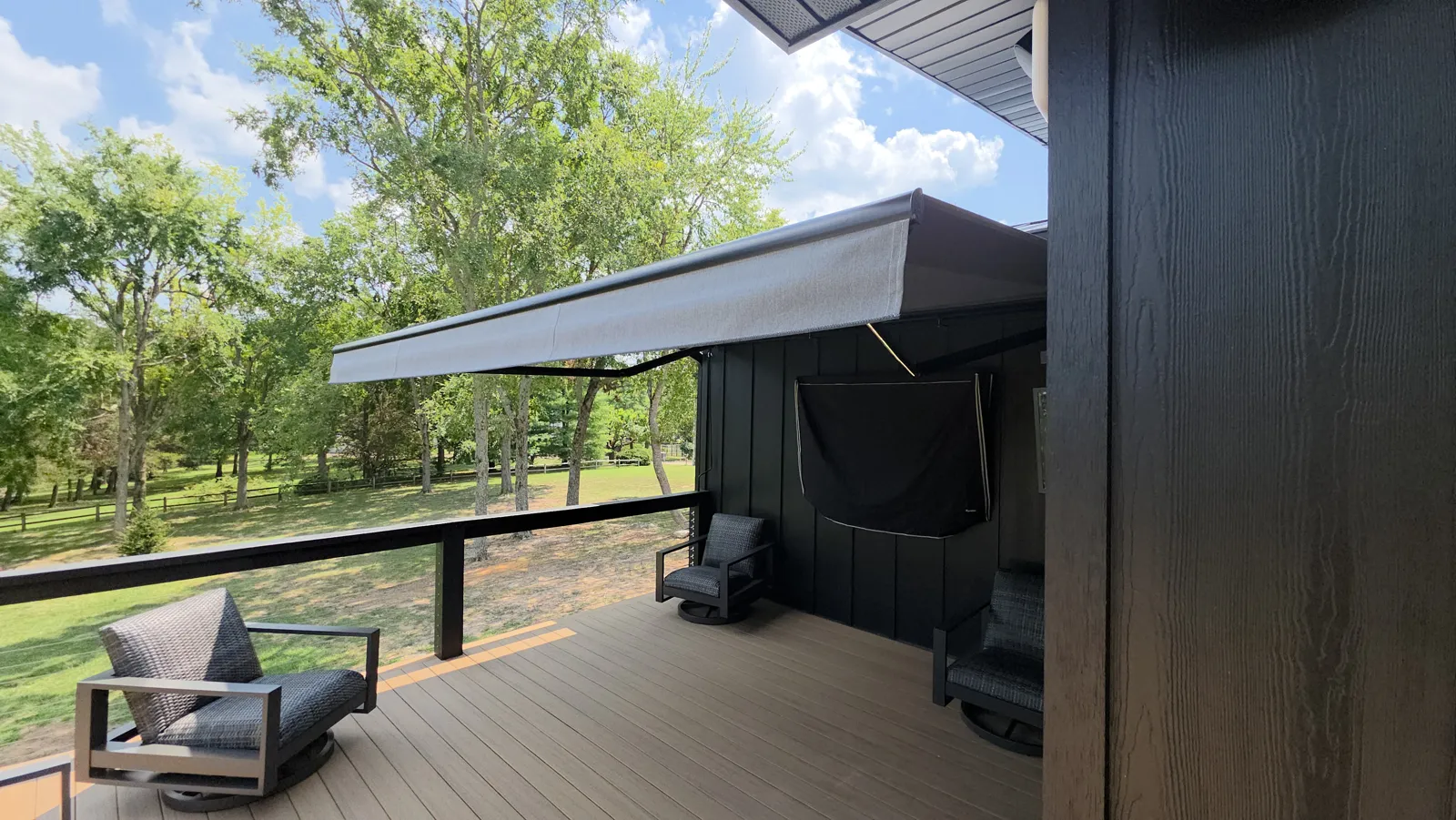 Charcoal retractable awning over a deck with black board siding and trees behind in Larue Acres, Rogers, Arkansas