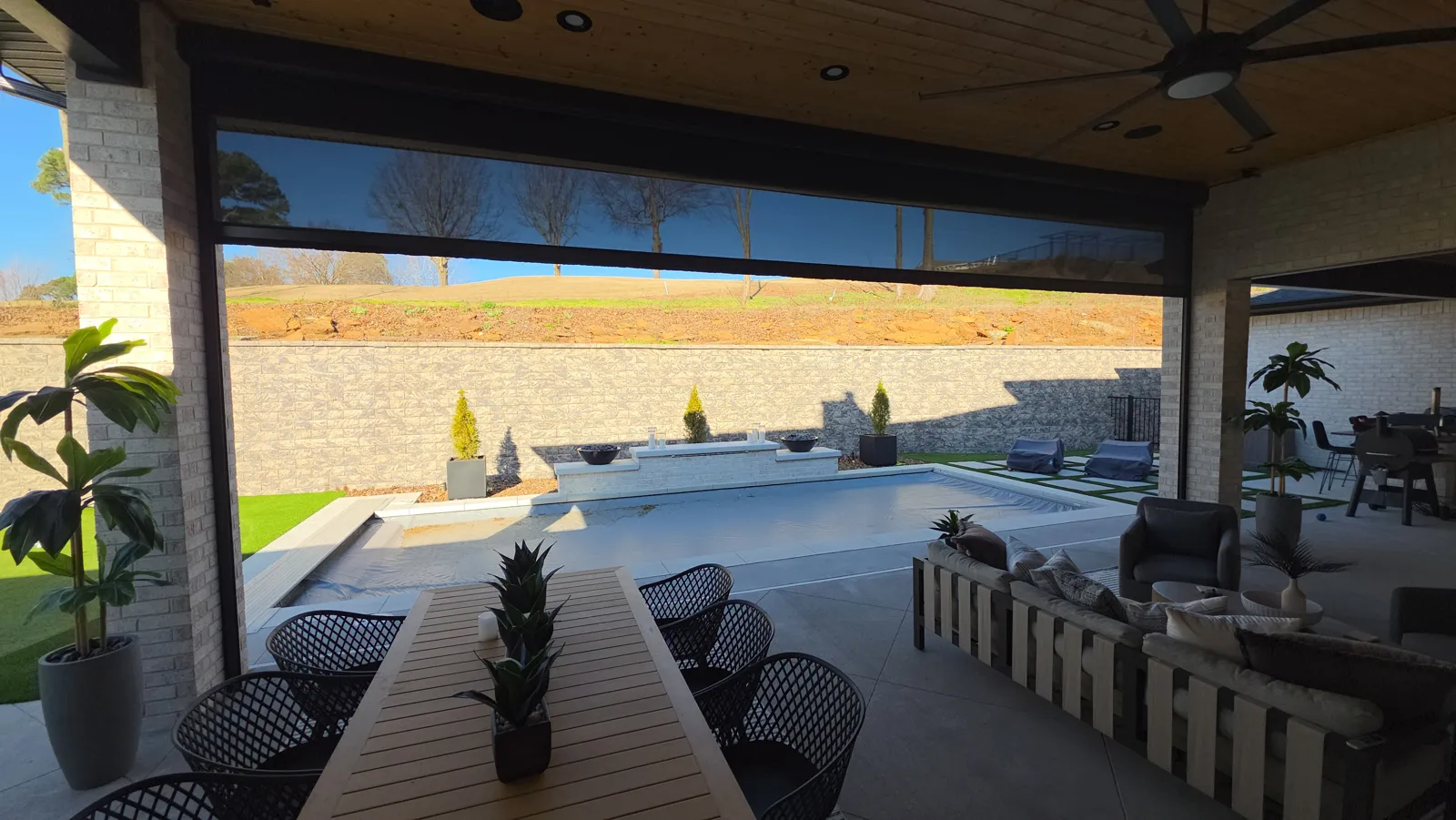 Dark screen lowered under a pine ceiling looking out to the pool with brick columns on each side in Masters, Fayetteville, Arkansas
