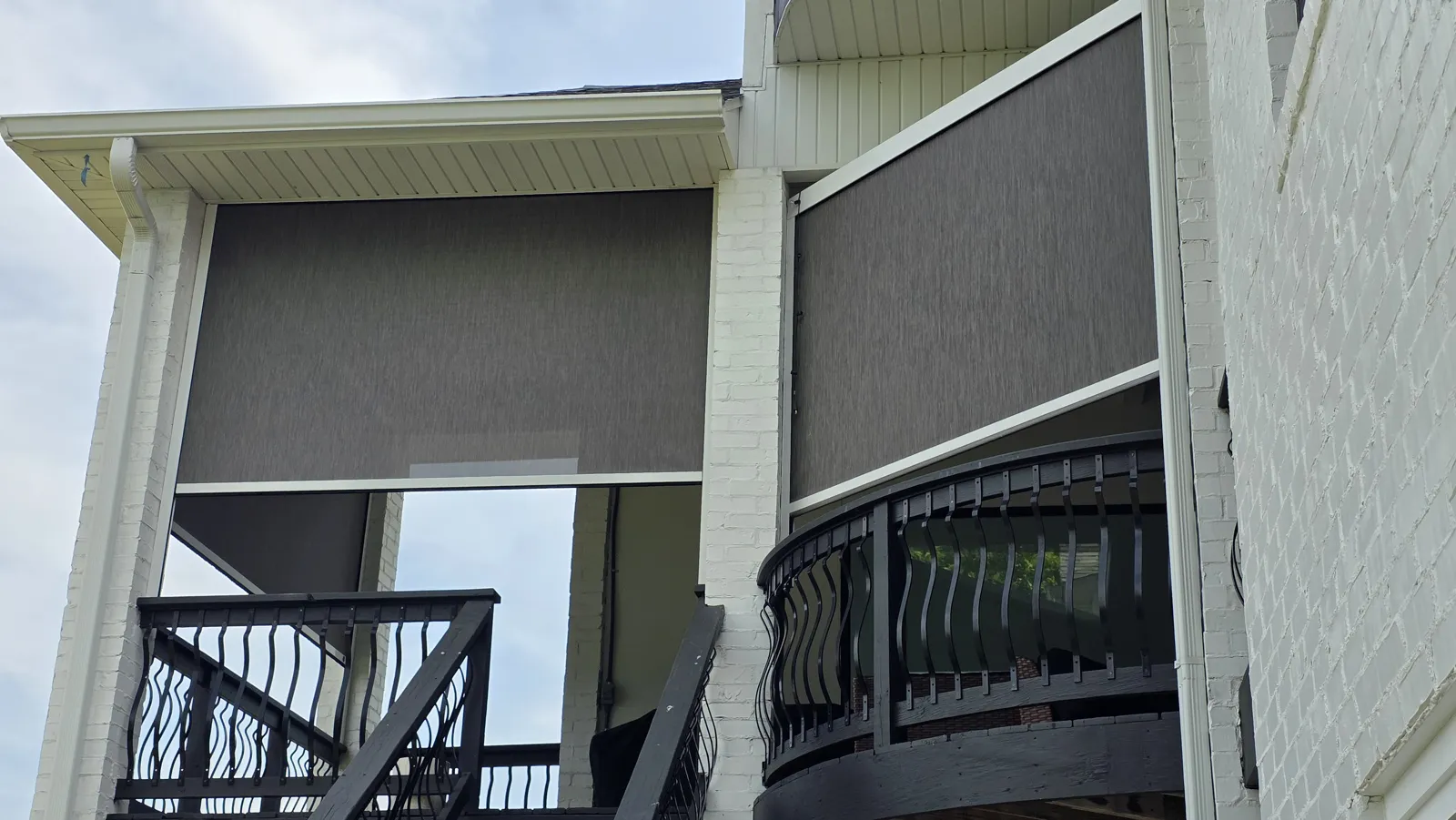 Gray screens on upper-level covered balcony openings with curved black railing on white painted brick in Otter Creek Estates, Cave Springs, Arkansas