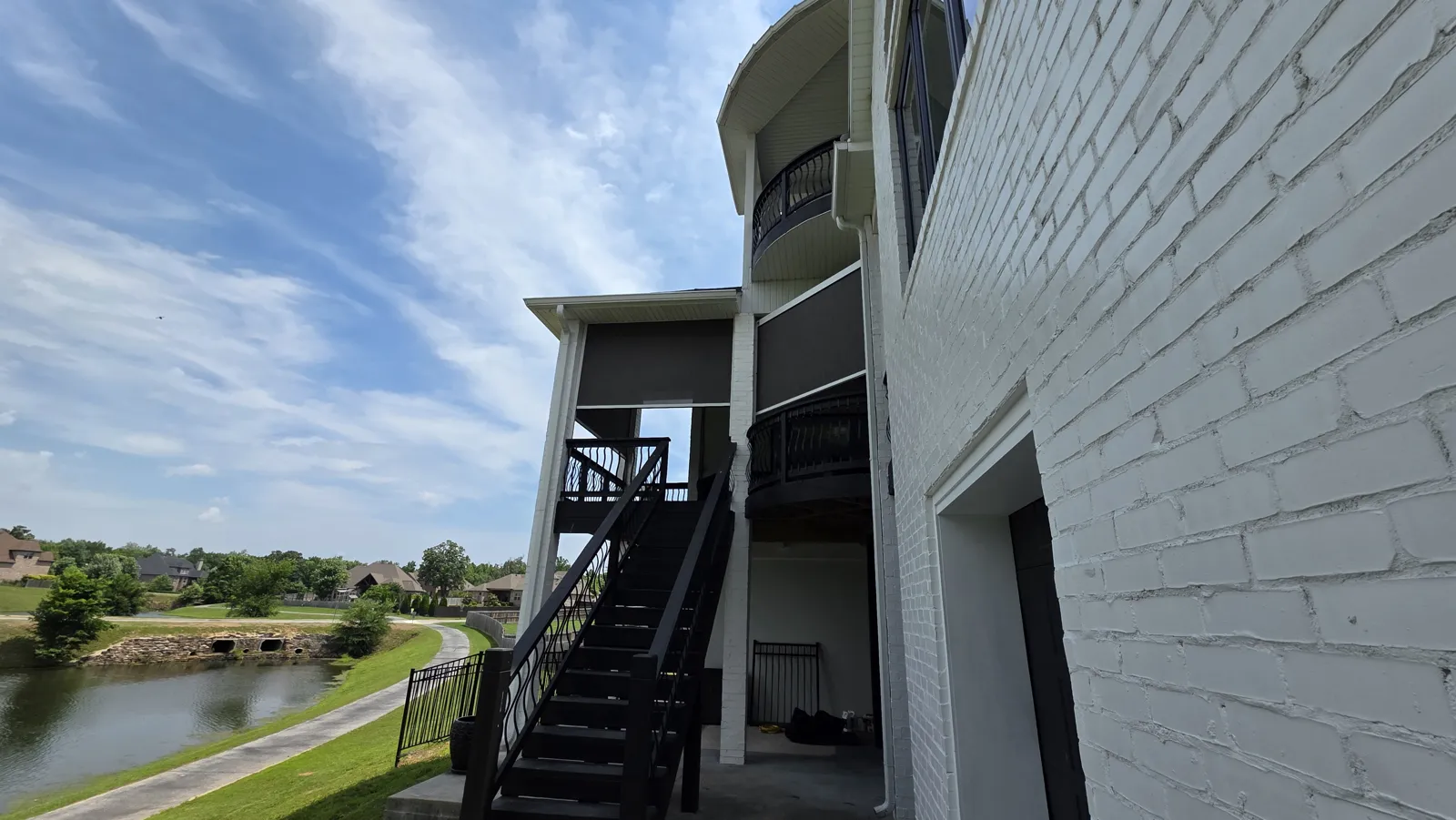 Gray screens on a two-story white painted brick house above a pond in Otter Creek Estates, Cave Springs, Arkansas