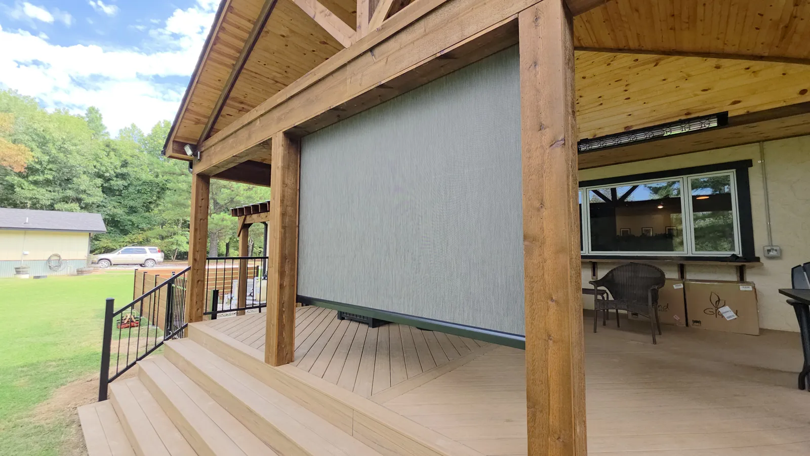 Gray screen closed beside heavy cedar posts on a covered deck with trees behind in Ozark Acres, Cave Springs, Arkansas