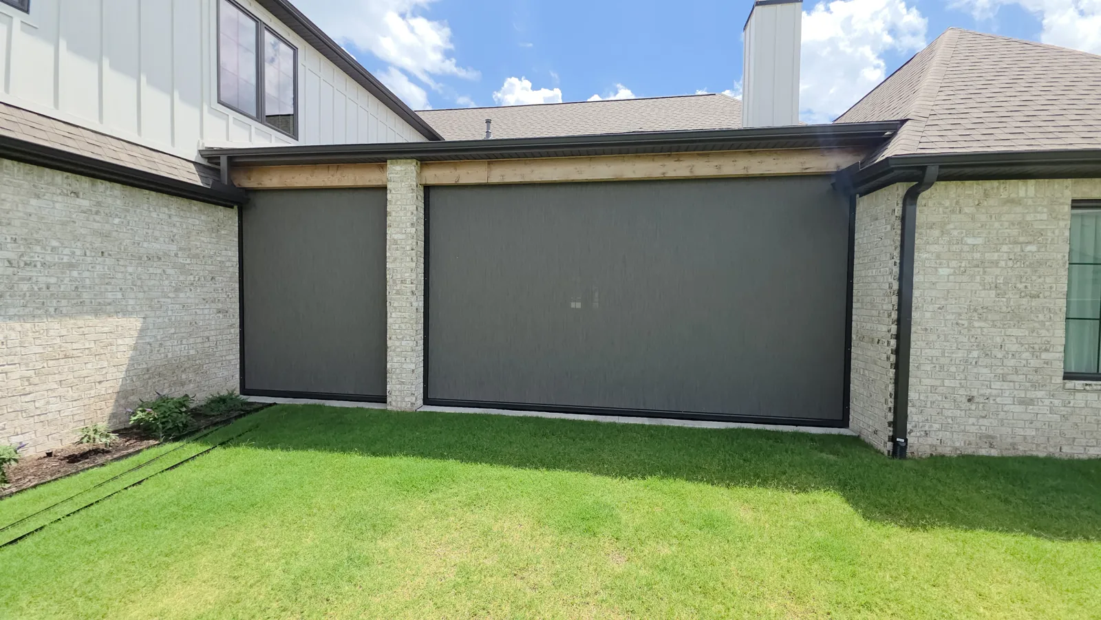 Two gray screens closed under a wood header on a white brick house with board-and-batten siding, over a green lawn, retractable screens for homes in Clear Creek, Johnson, Arkansas