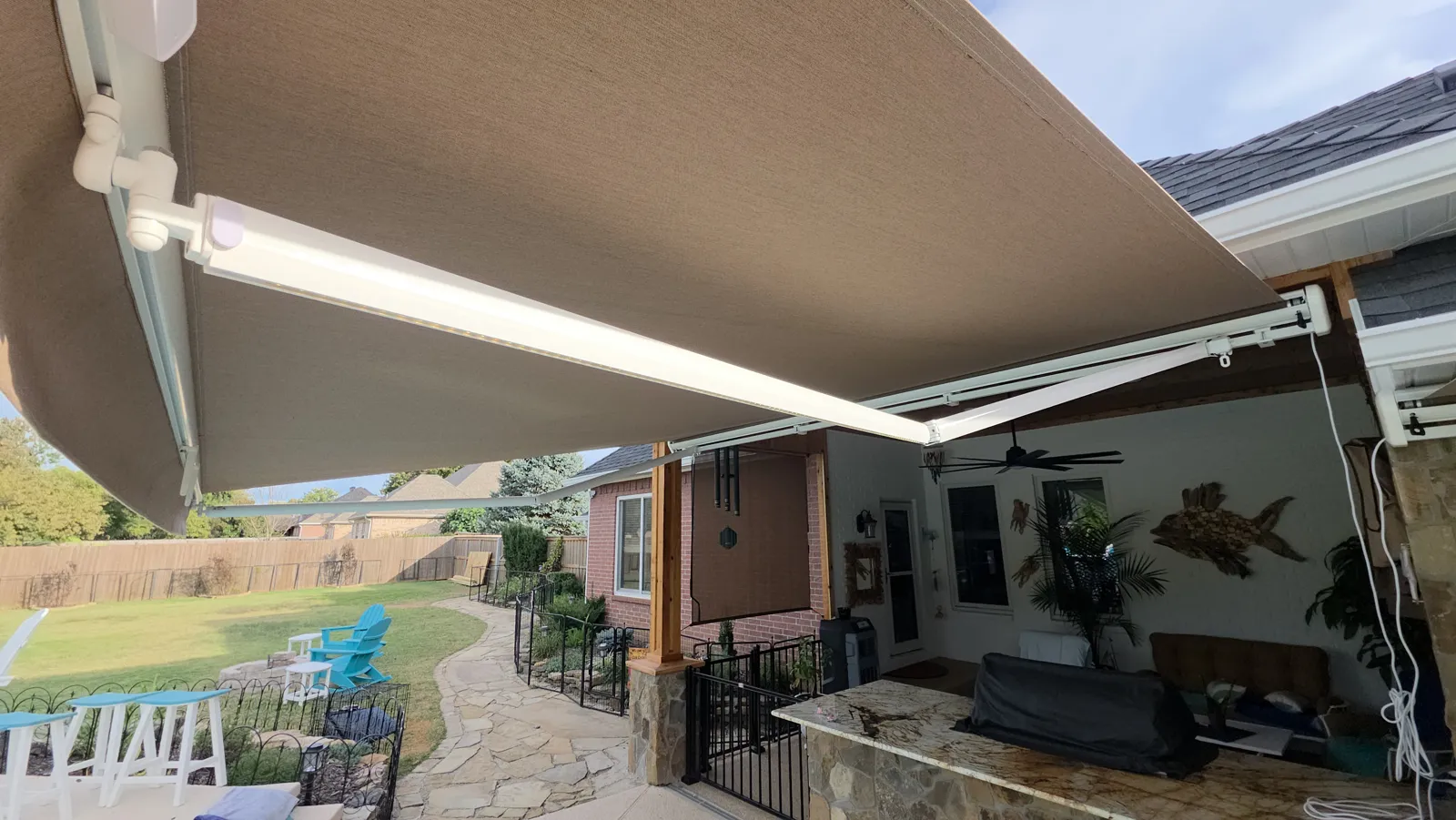 Underside of a tan fabric retractable awning with white arms over a patio, stone path and lawn in Silverthorne, Fayetteville, Arkansas