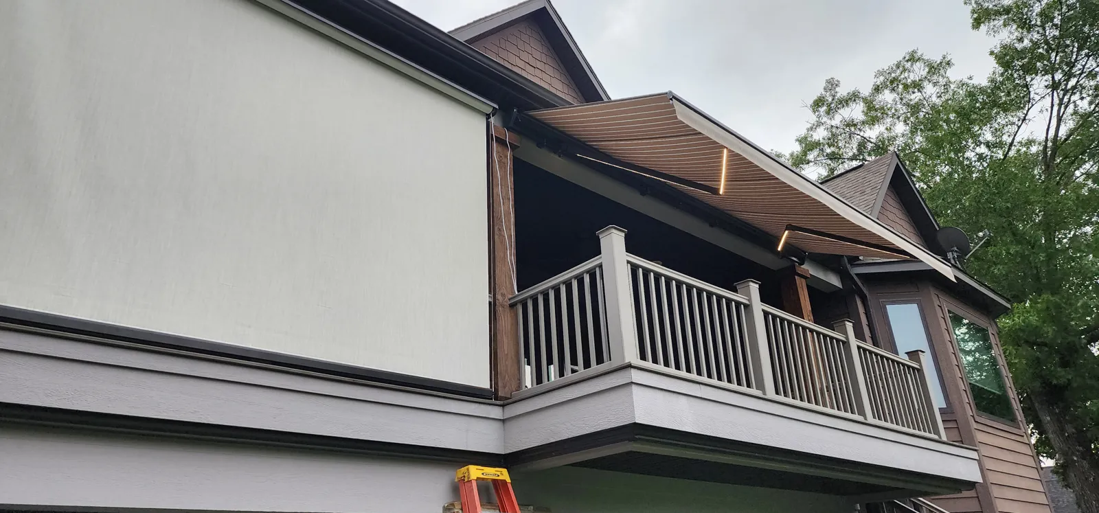 Light gray retractable screen closed on an upper deck with white railing, with a retractable awning beside it in The Estates of Lakeway, Rogers, Arkansas