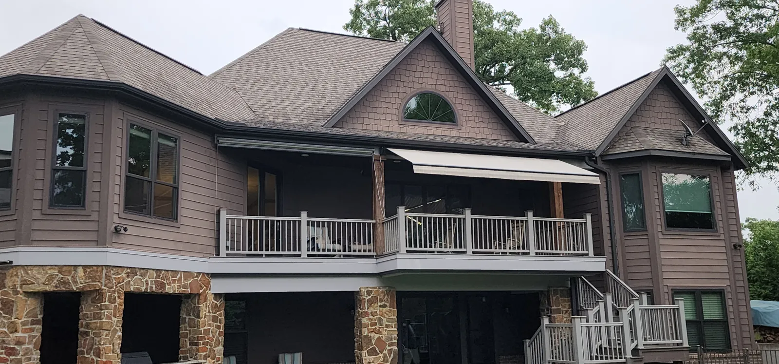 Back of a brown sided house with a screen and a retractable awning on the upper deck, stone base below in The Estates of Lakeway, Rogers, Arkansas