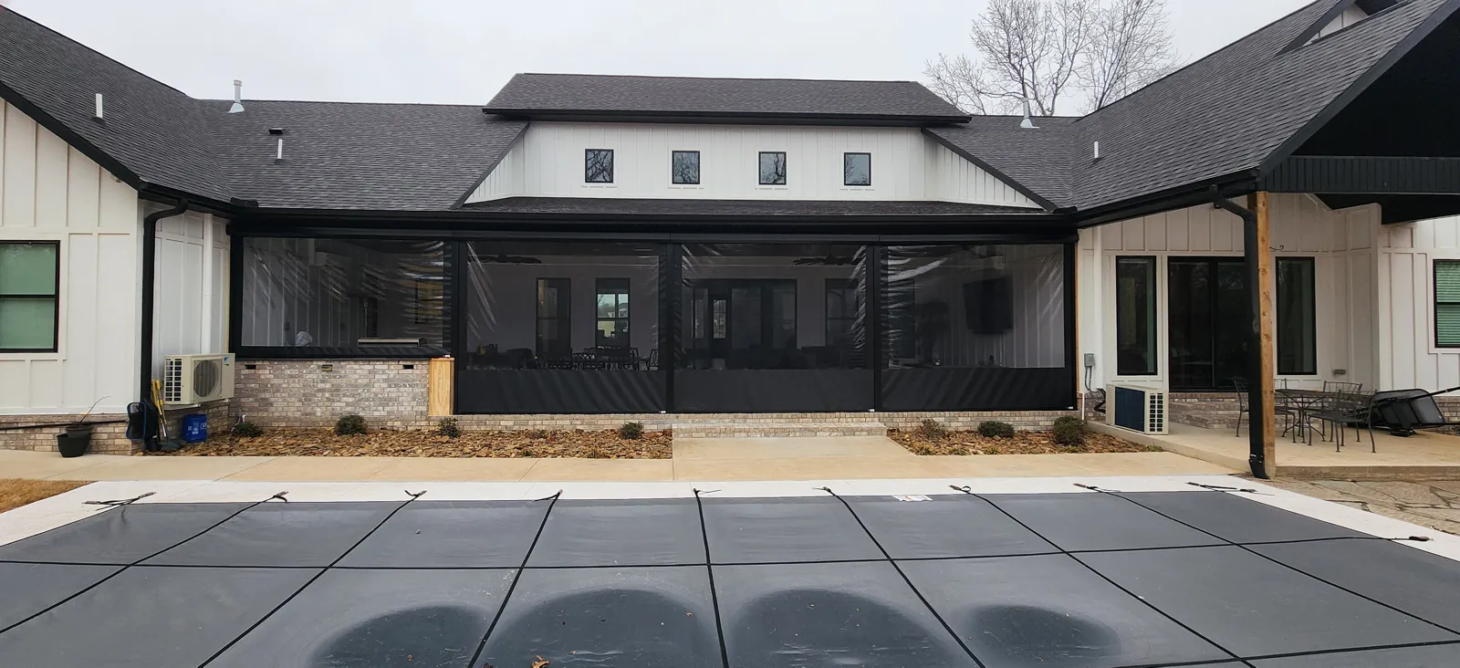 Black screens across the wide covered back patio of a white house with the pool cover in front in The Meadows, Little Flock, Arkansas