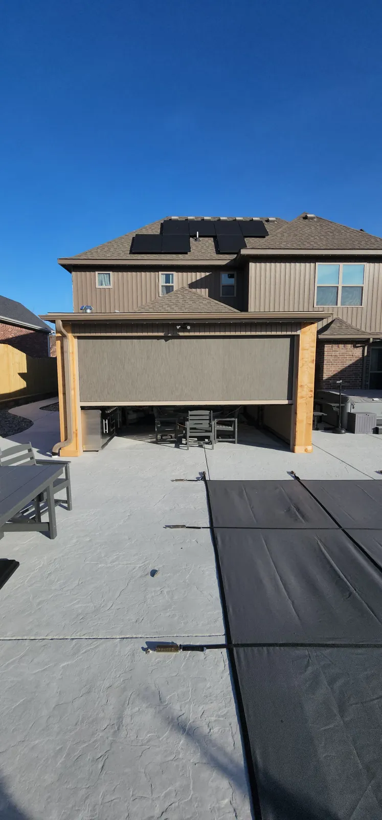 Taupe screen closed across a cedar-post patio cover with the pool cover in front in The Peaks, Rogers, Arkansas