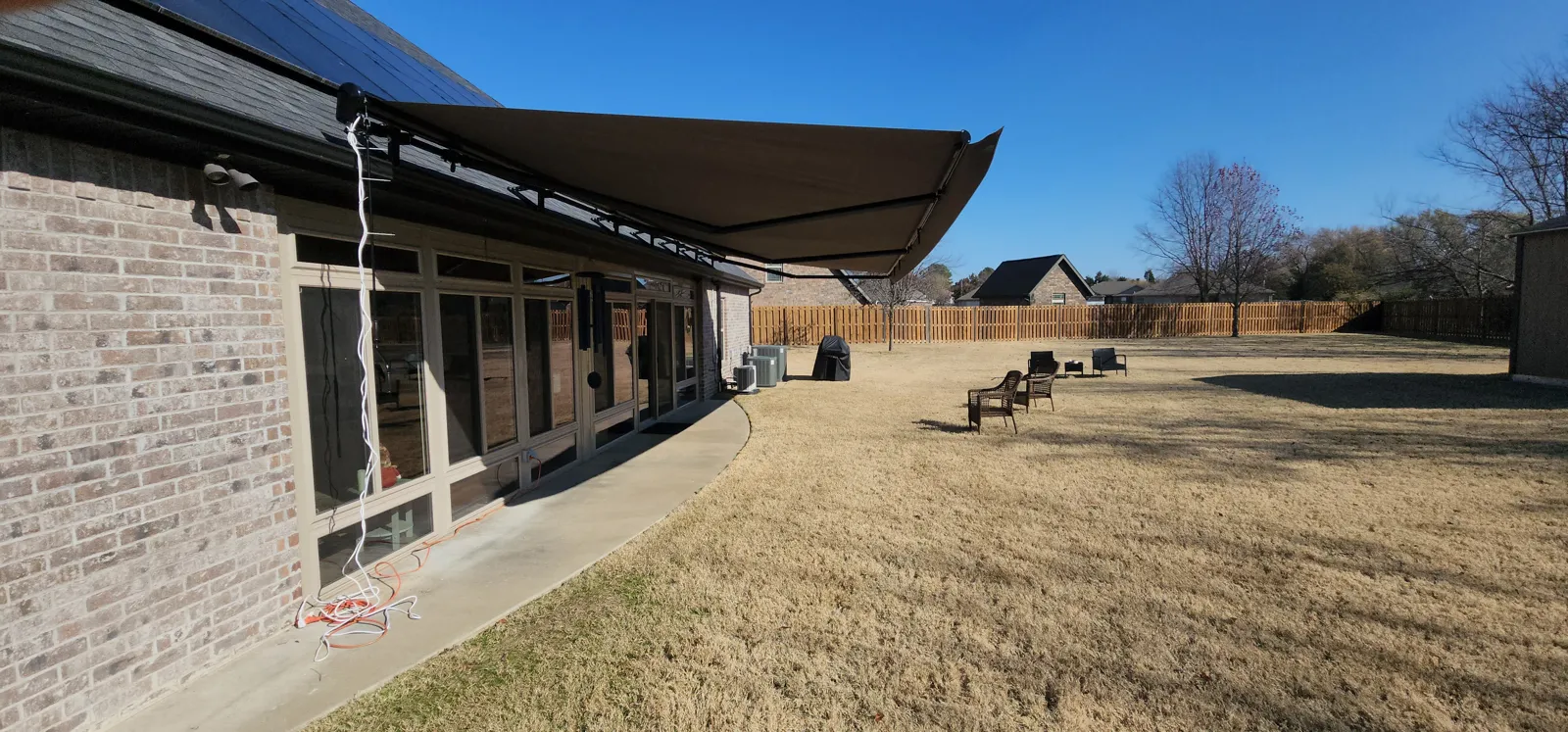 Dark brown retractable awning along the back of a brick house with a long lawn in Thornbury, Springdale, Arkansas