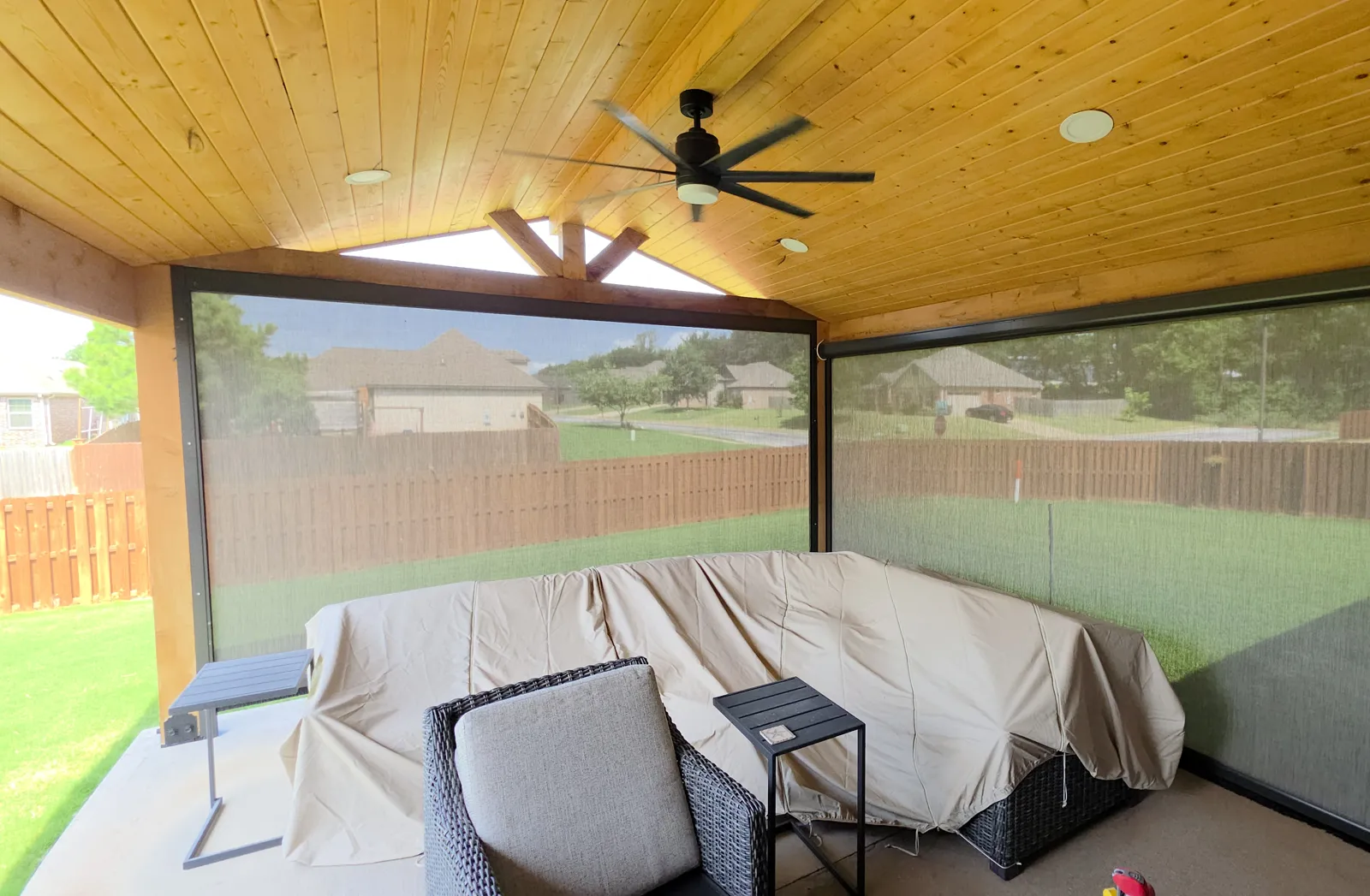 Gray mesh closed across a covered patio with a pine ceiling and ceiling fan, wood fence behind in Weatherton, Lowell, Arkansas