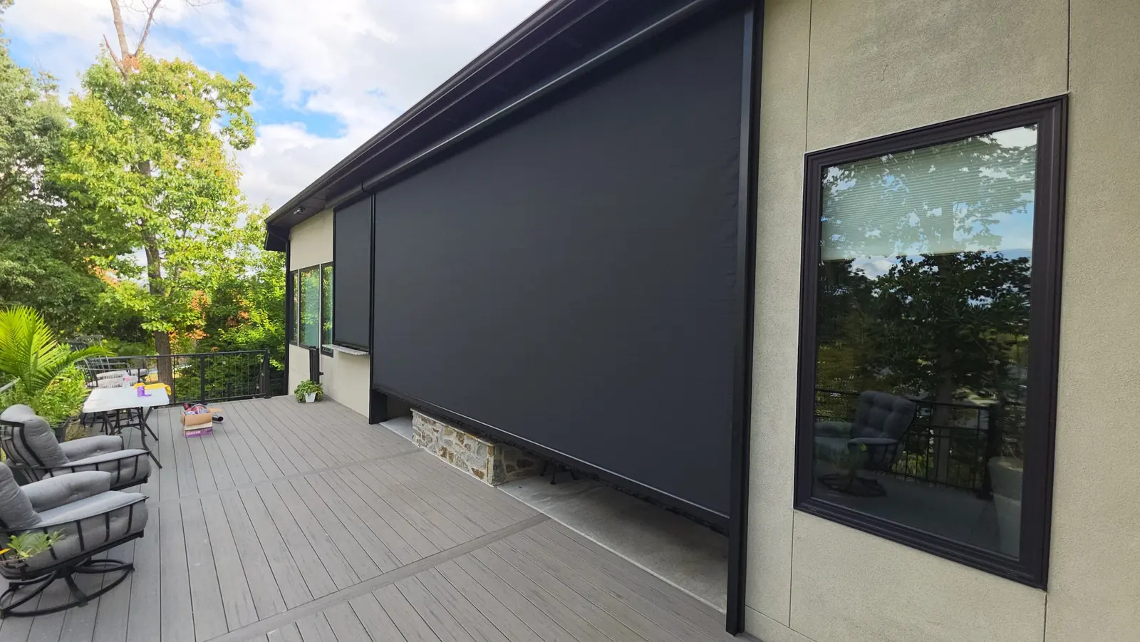 Flat black motorized retractable screen fully down on a covered deck in Rogers, Arkansas, black housing mounted above the header