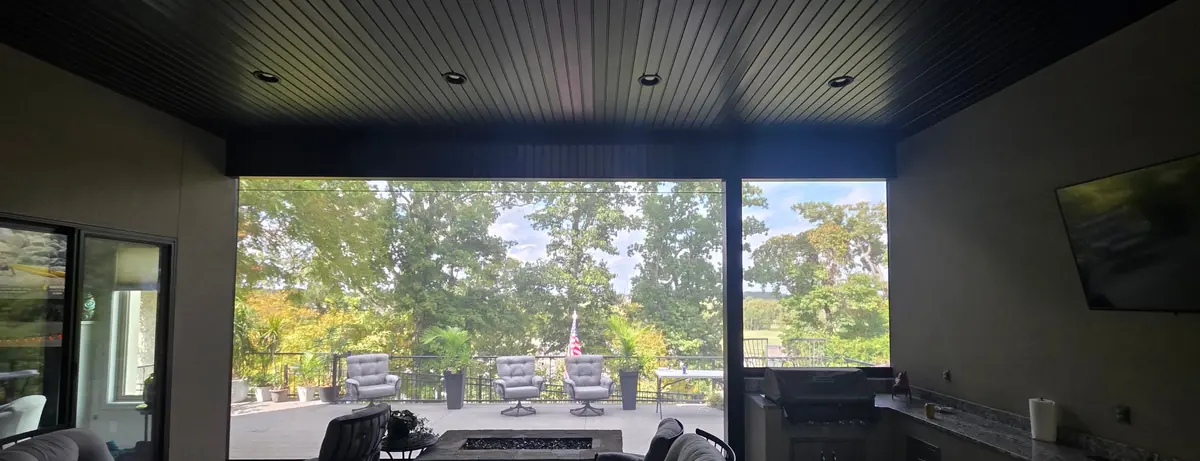 View from inside the same Rogers patio with the flat black motorized screen down, trees, deck and flag still visible
