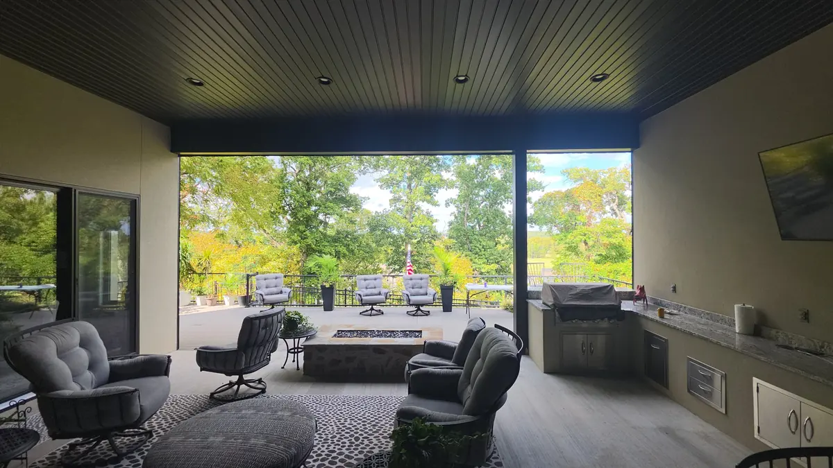 View from inside a covered patio in Rogers, Arkansas with the motorized screen raised, showing the deck, trees and fire pit